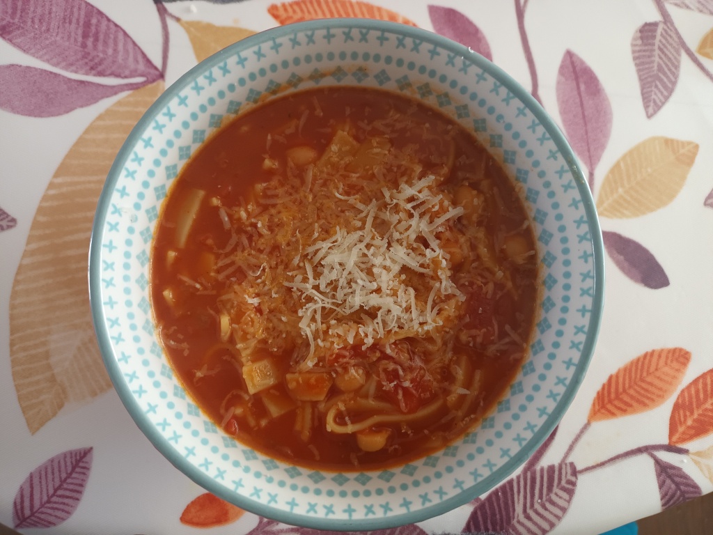 A bowl containing a red, tomato soup topped with grated Parmesan cheese. 