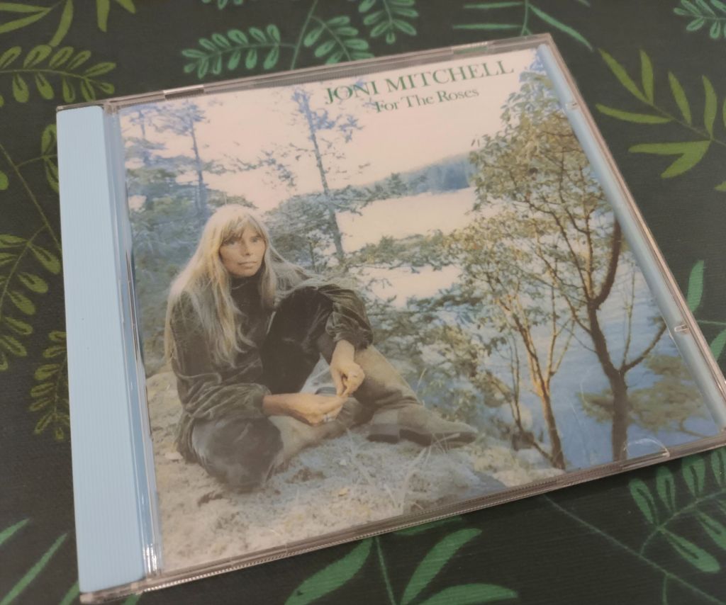 CD of Joni Mitchell's album For the Roses. The cover features a photograph of the artist sitting outside with a lake and trees in the background. 