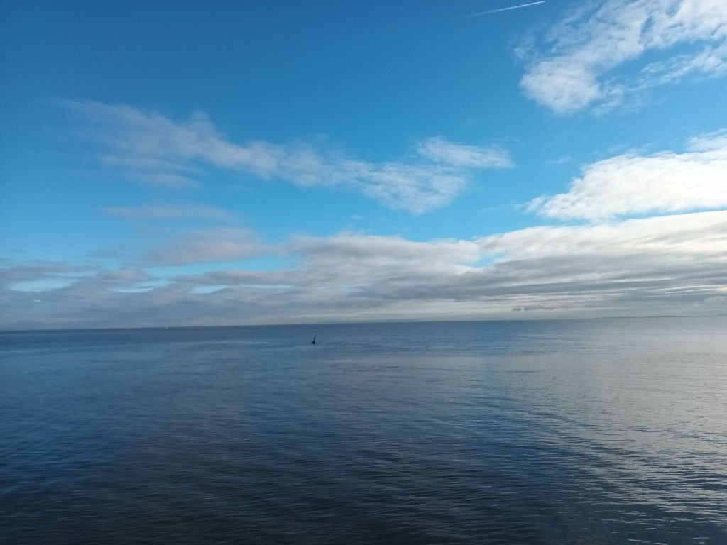 A view of the sea on a calm day with a blue sky and fluffy white clouds above. 